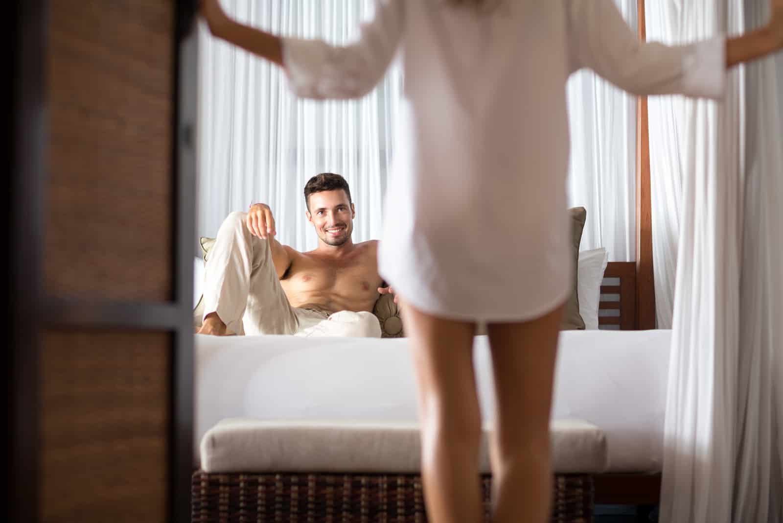 uomo seduto sul letto che guarda la donna con la sua camicia