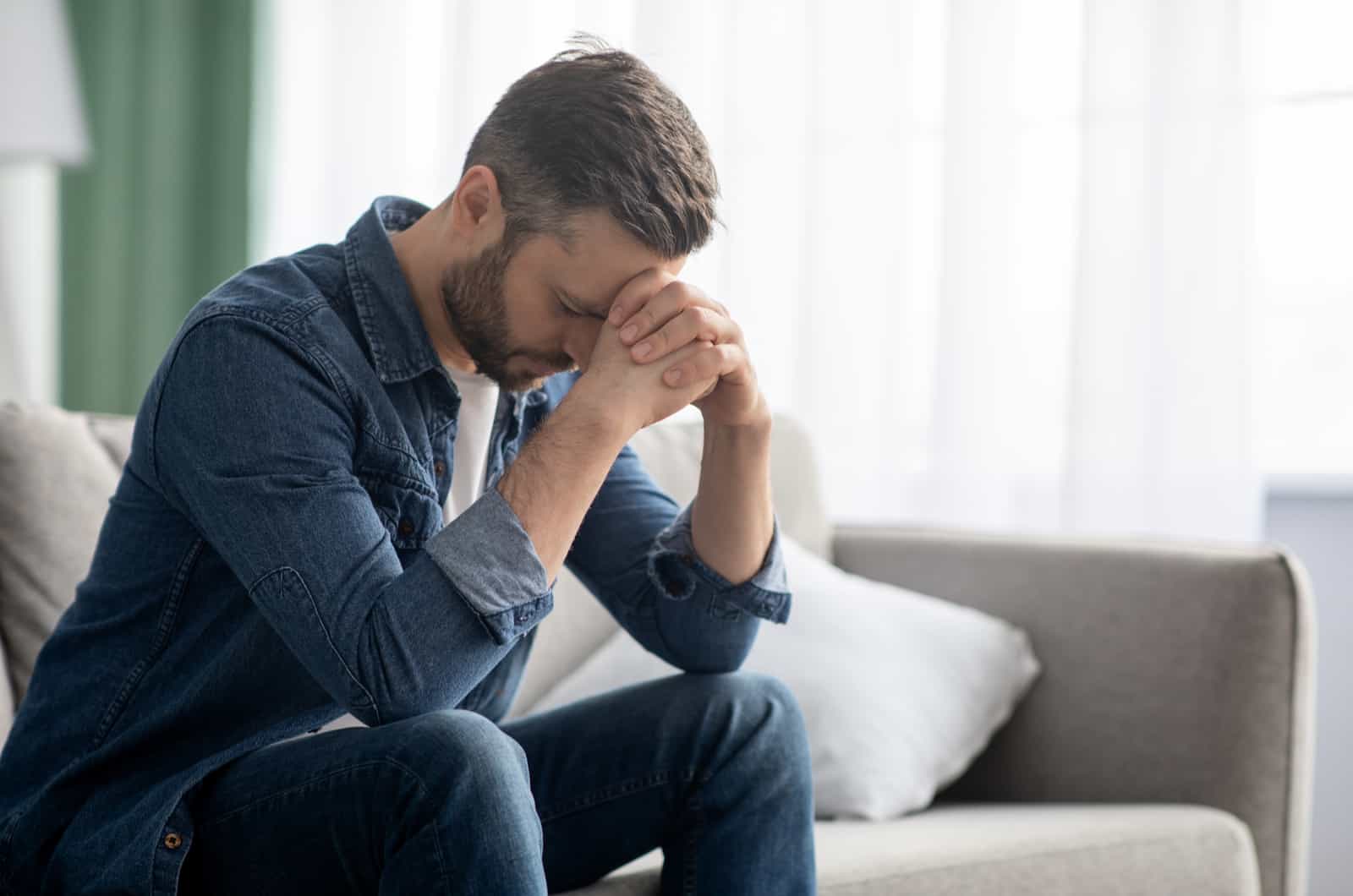 uomo triste seduto sul divano con le mani sul viso