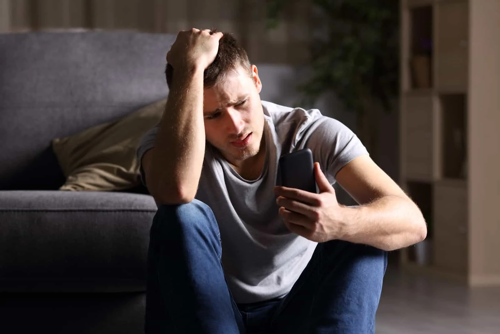 sad young man sitting on the floor and looking at mobile phone