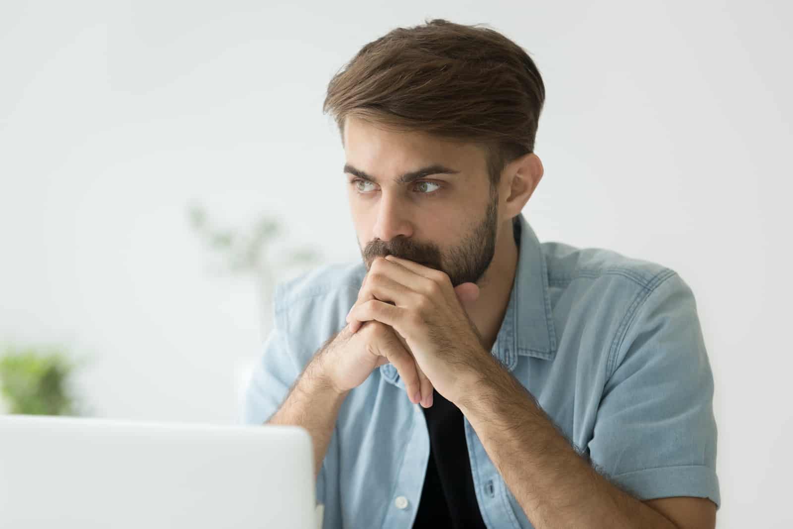 homem sério sentado junto ao computador portátil em pensamentos profundos