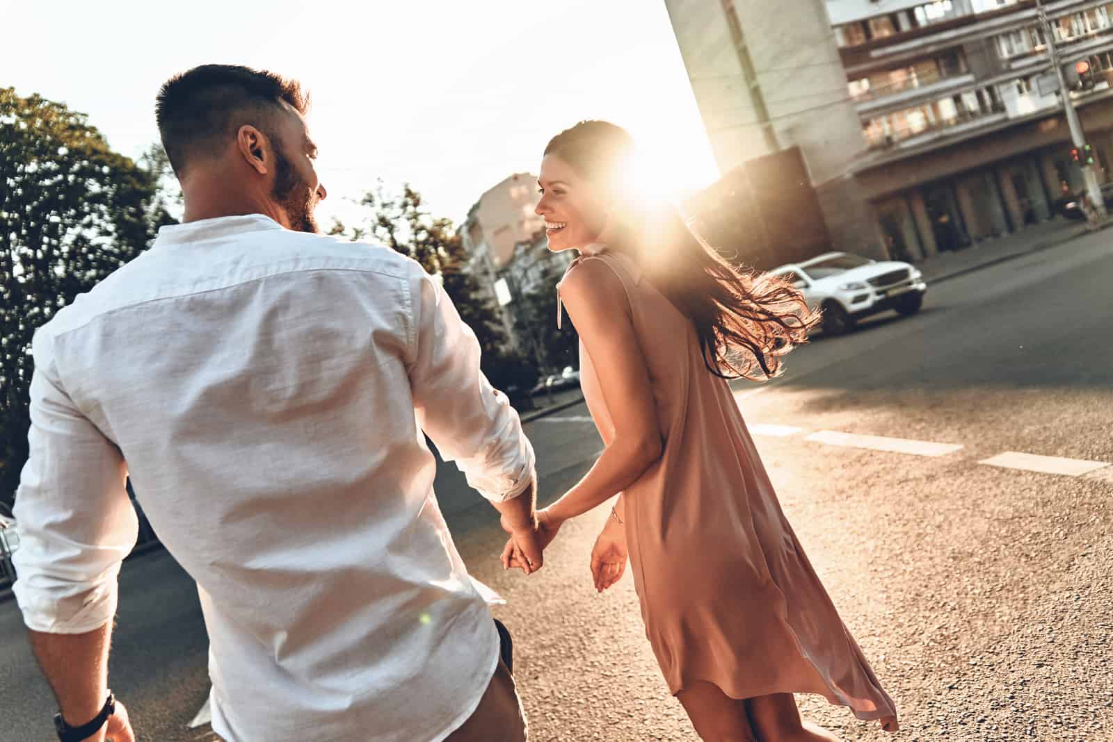 sonriente pareja de enamorados caminando por la calle cogidos de la mano