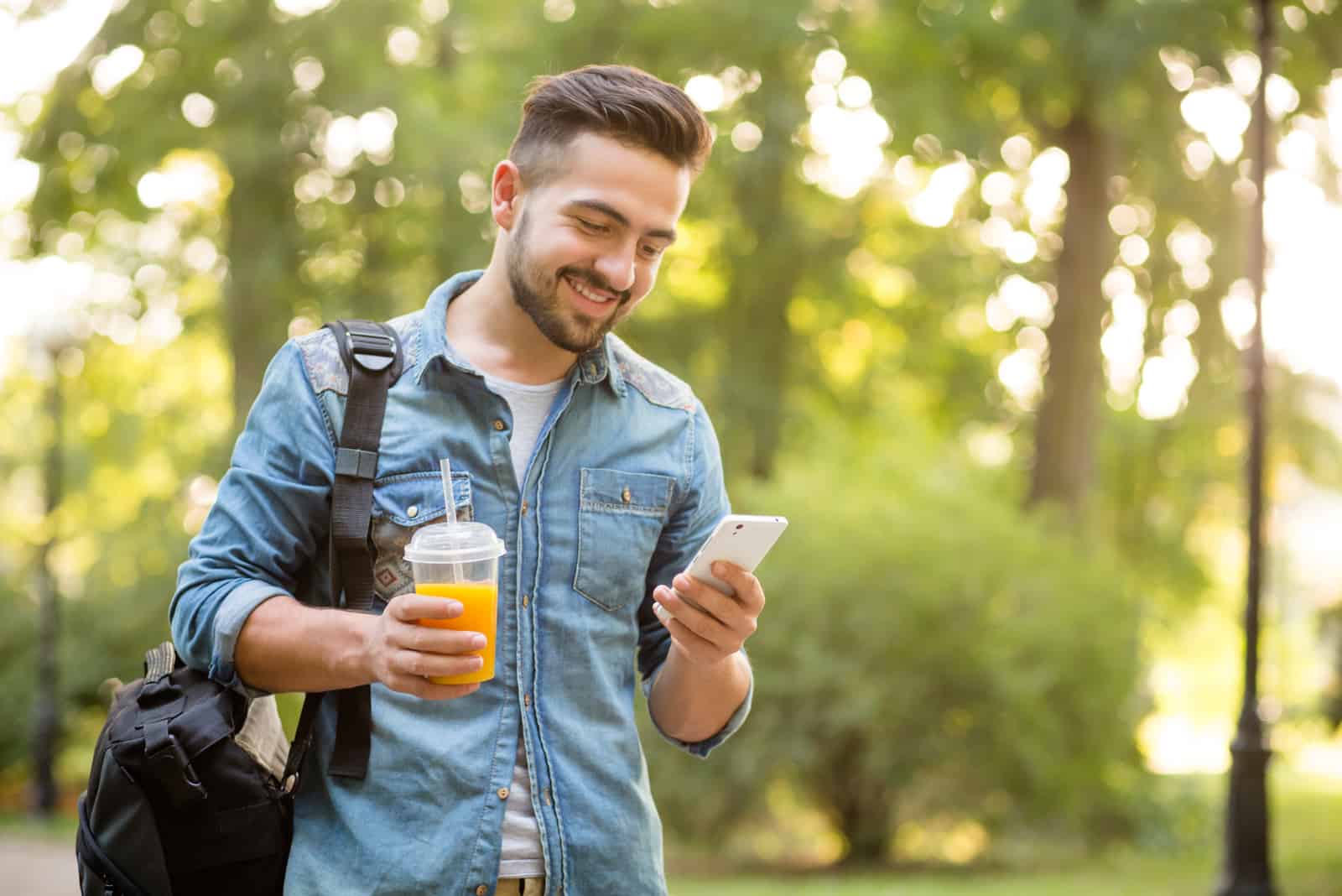 Uomo sorridente che tiene un succo di frutta in una mano e un telefono cellulare nell'altra