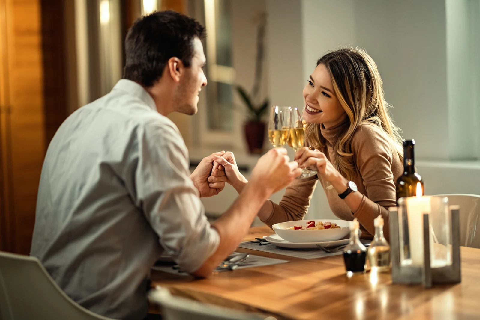 the man holds the woman's hand as they sit down to dinner