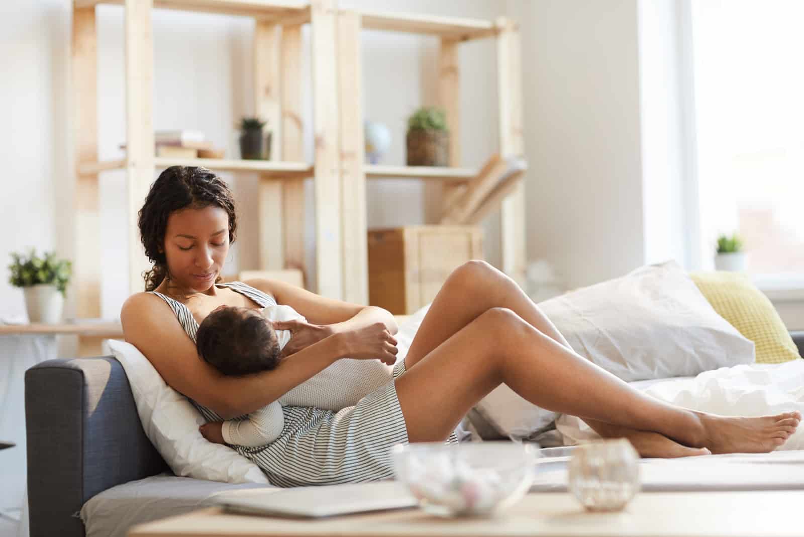 the woman lies on the couch and breastfeeds the child