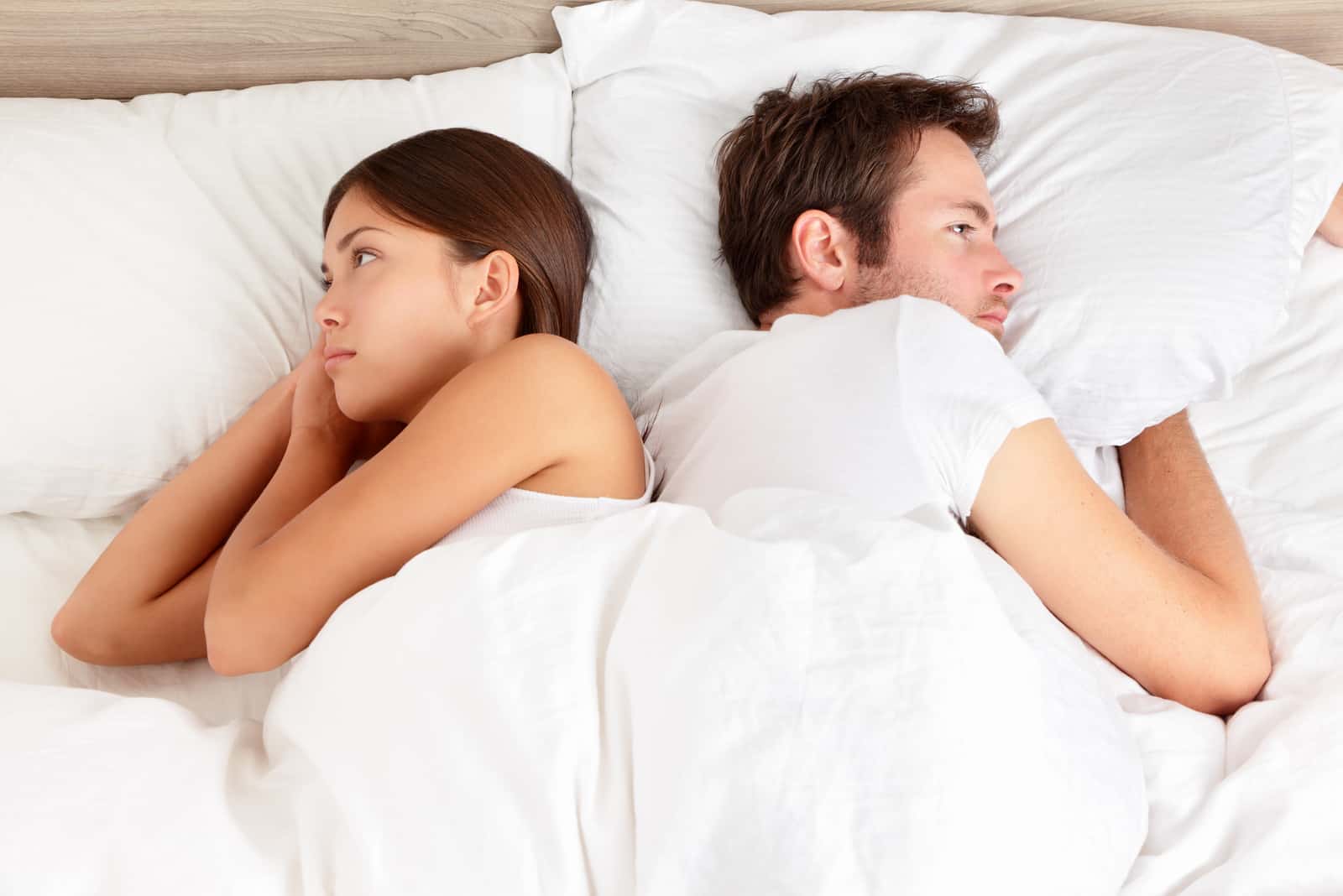 pareja infeliz tumbada en la cama en sus lados opuestos