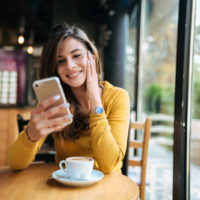happy woman looking at mobile phone at cafe