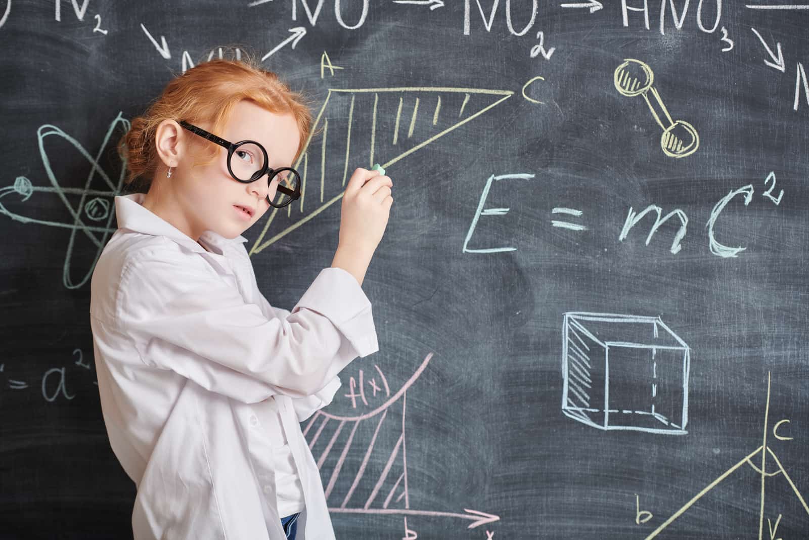 A smart little girl writes formulas and diagrams on the blackboard