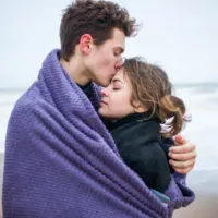 man kissing woman's forehead wrapped into blanket
