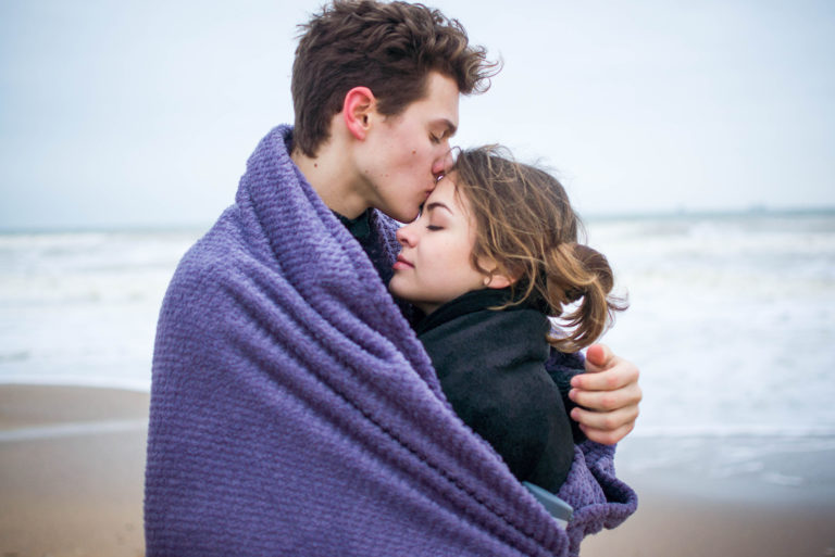 man kissing woman's forehead wrapped into blanket
