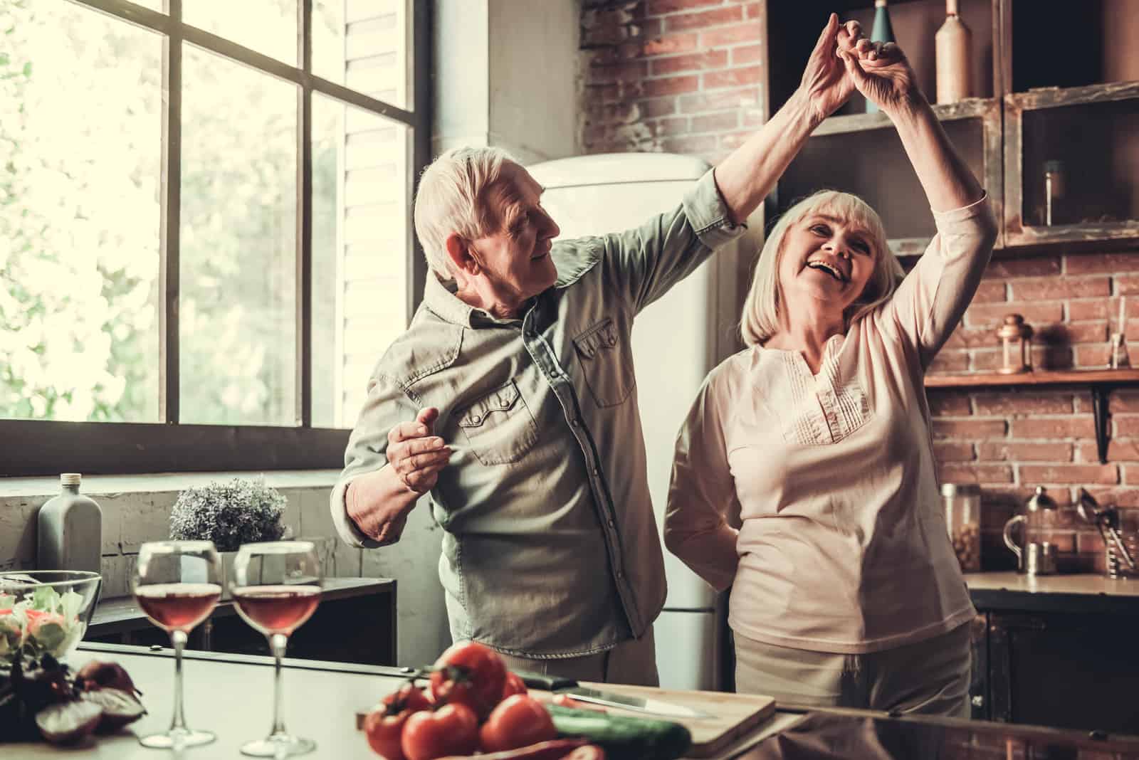 Bella coppia di anziani sta ballando e sorridendo mentre cucinano insieme in cucina