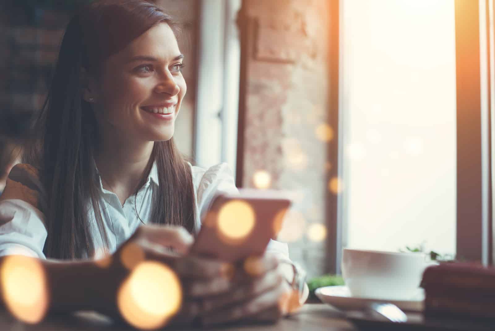Donna sorridente in un caffè che usa il cellulare