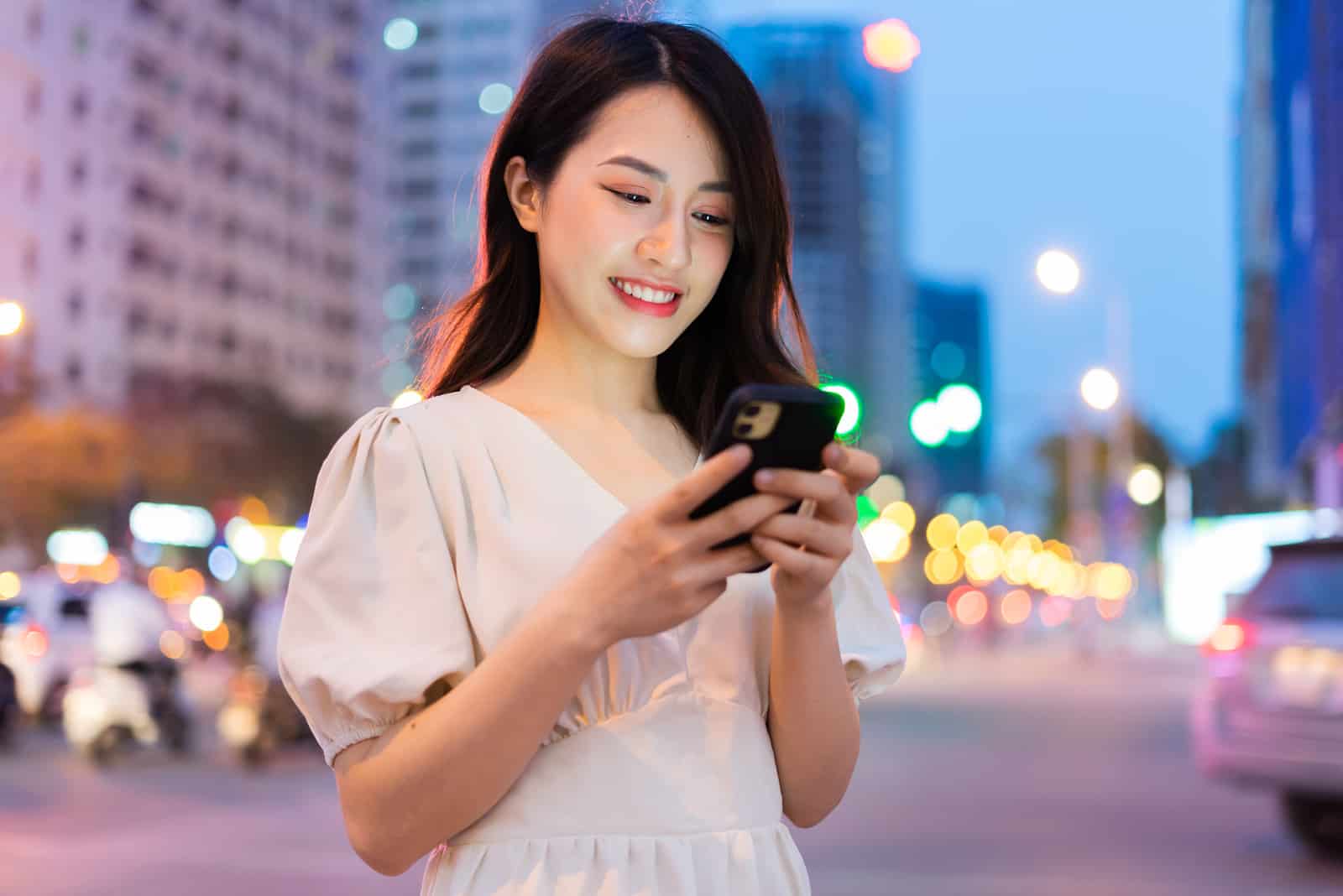 Mujer joven utilizando un smartphone en la calle por la noche