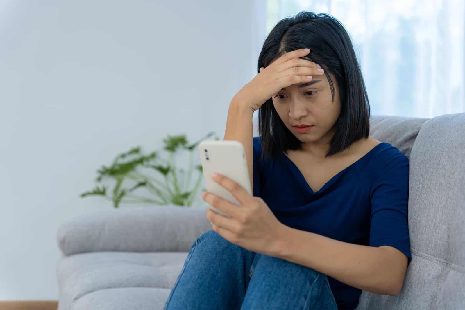 confused woman sitting on sofa with phone in hand