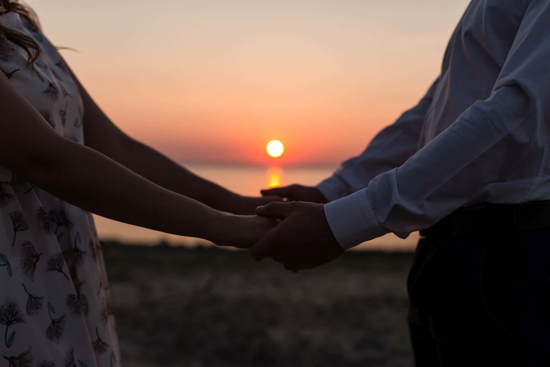 couple holding hands with sunset in background
