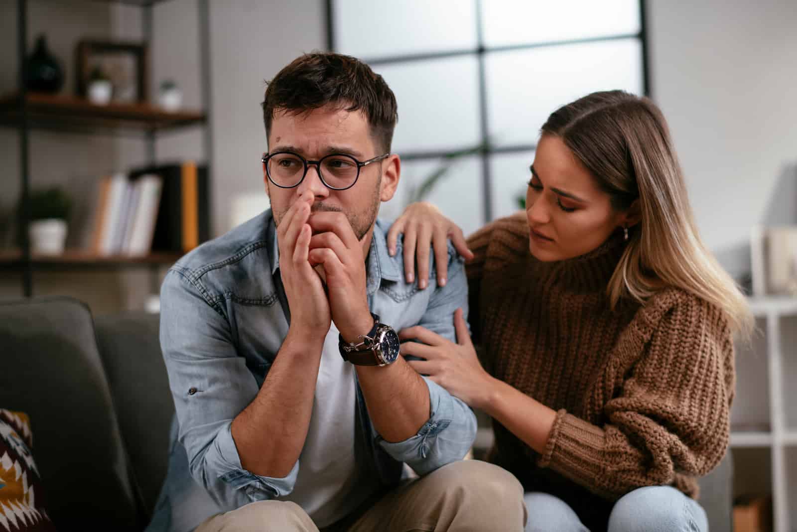 casal sentado no sofá enquanto a namorada conforta o homem