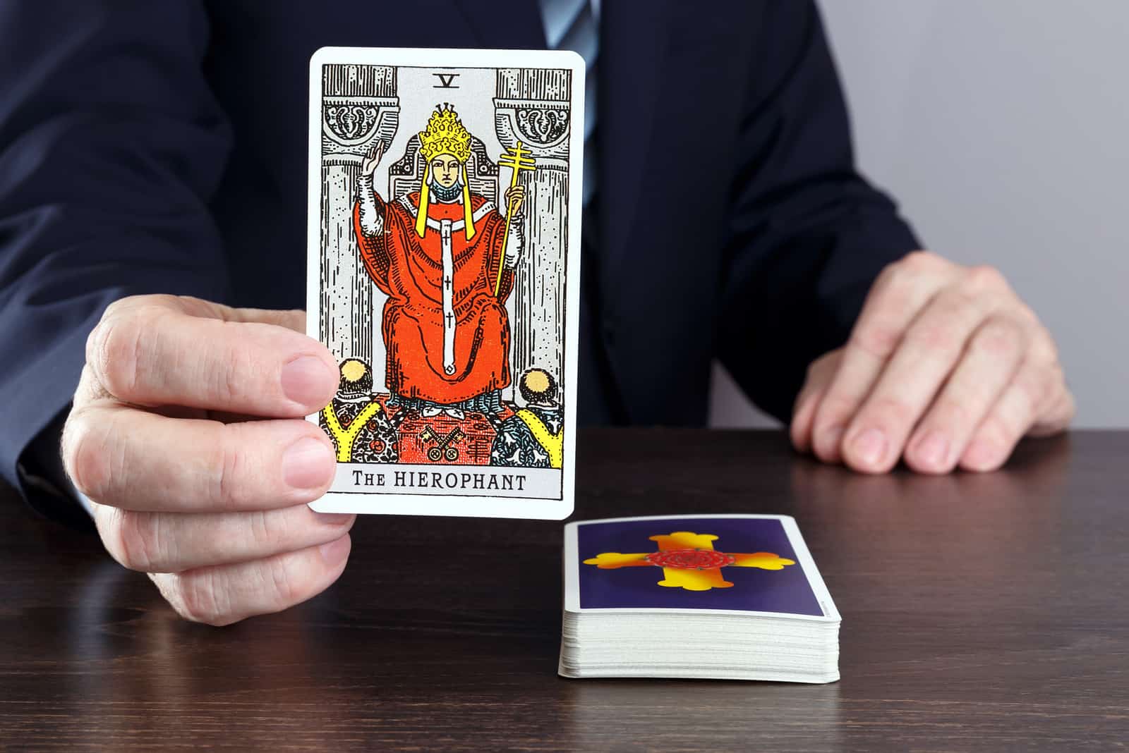 man holding the hierophant tarot card above the table