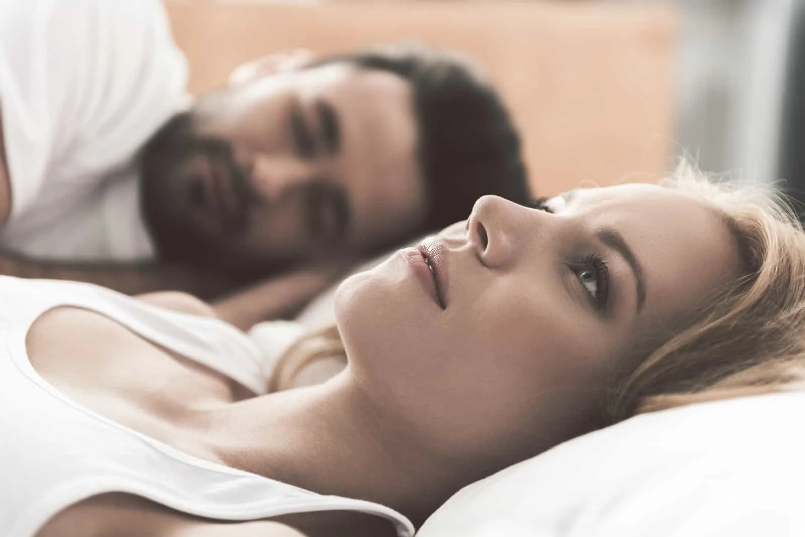 sad woman lying in bed while man is sleeping