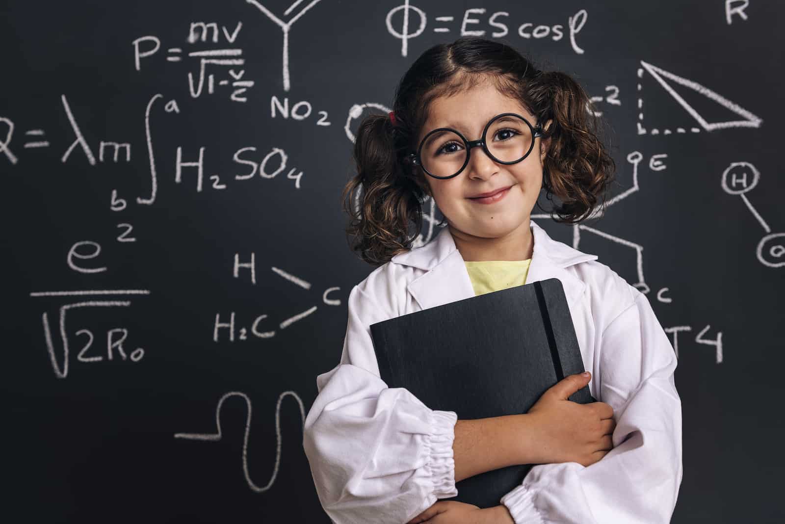 niña sonriente con bata de laboratorio y un cuaderno