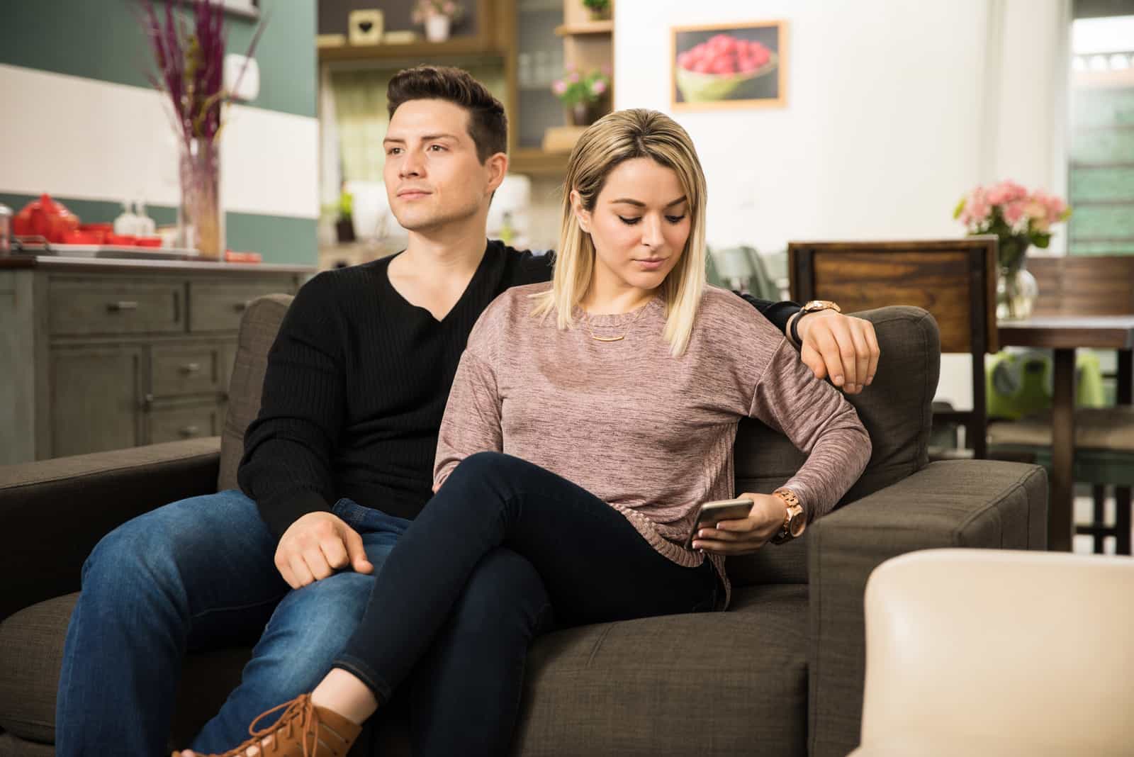 mujer enviando un mensaje de texto a su amante mientras está sentada junto a su novio en casa