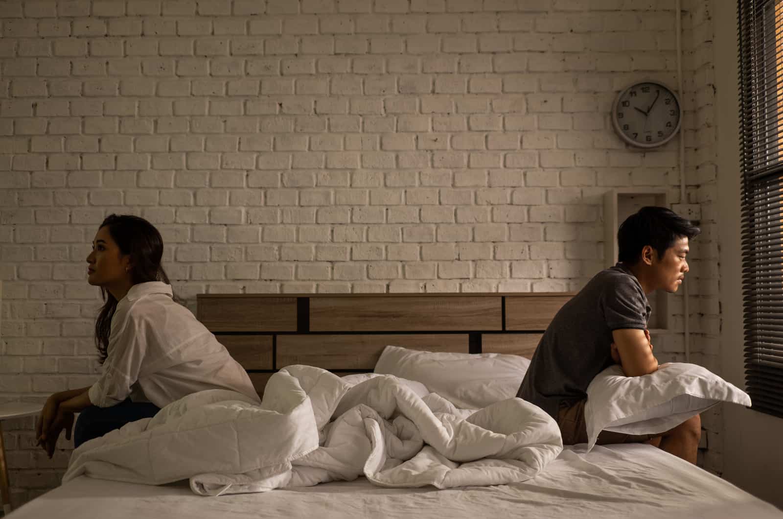 young couple sitting apart on bed