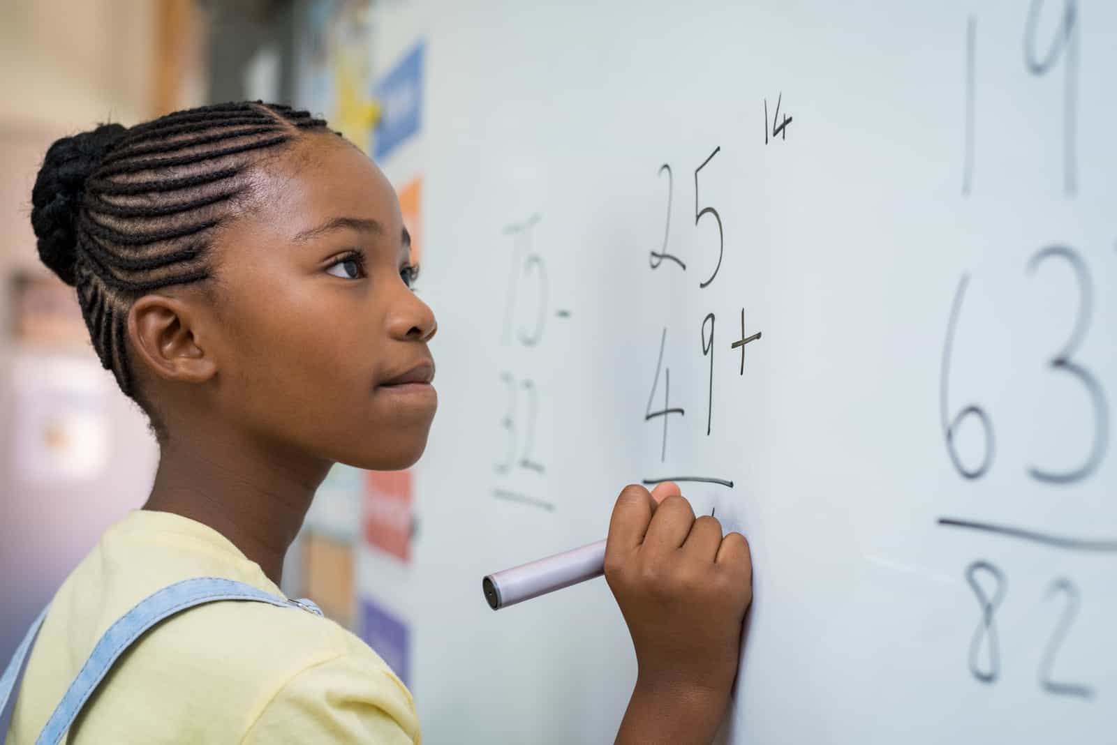 young girl writing a mathematics sum on the blackboard