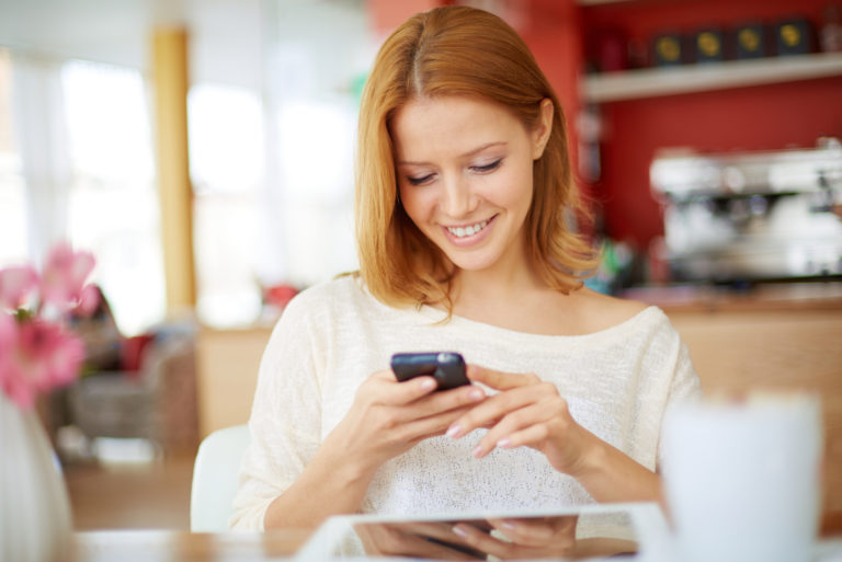 a smiling woman sitting at a table holding a cell phone in her hand