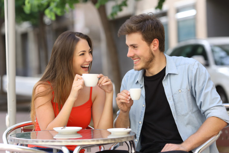 un hombre y una mujer sonrientes sentados al aire libre tomando café hablando