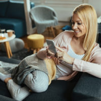 a smiling woman sits on the couch and buttons on the phone