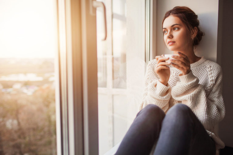 a beautiful woman is sitting by the window holding a salt shaker in her hand