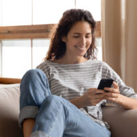 happy woman sitting on sofa texting
