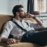 tired man sitting on sofa with drink in hand