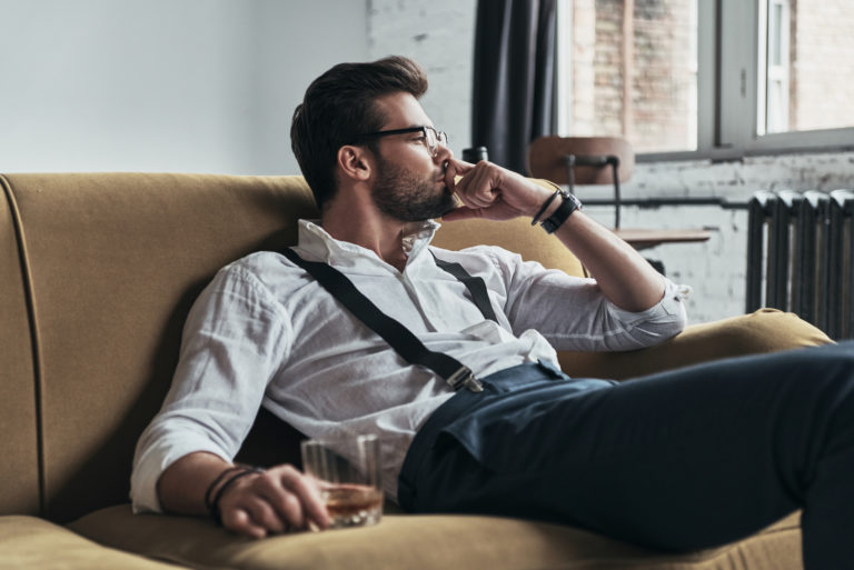 homem cansado sentado no sofá com uma bebida na mão