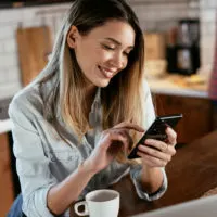 a smiling woman sitting at a table holding a cell phone in her hand