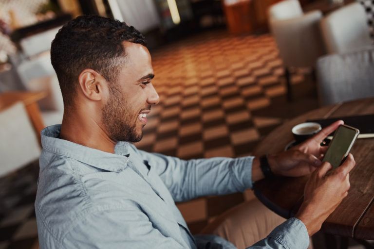 hombre sonriente enviando mensajes de texto en su teléfono móvil en el café