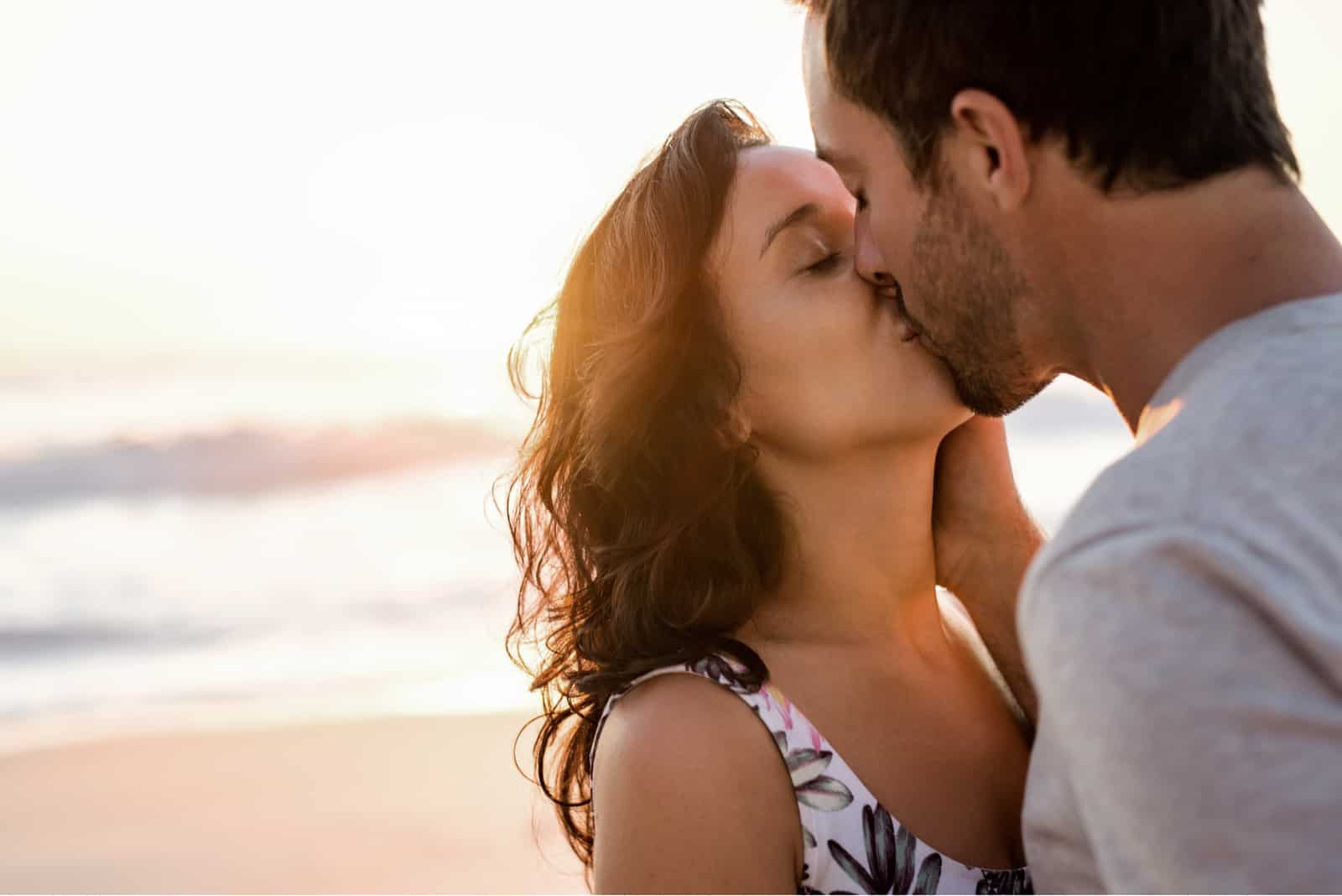 Pareja de jóvenes enamorados abrazados y besándose en una playa de arena al atardecer