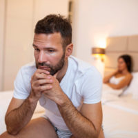 man sitting on bed with mad woman in background