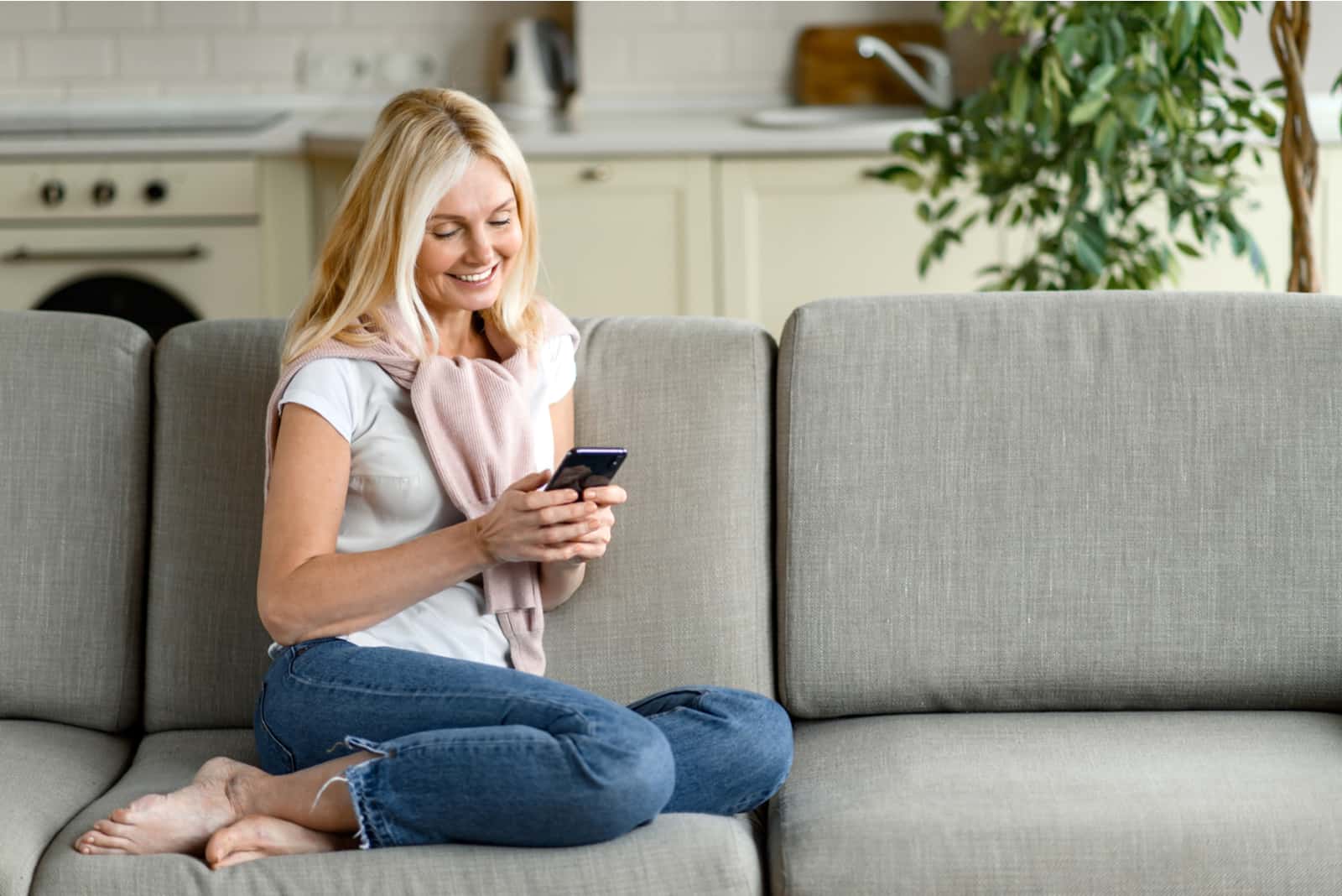a beautiful blonde haired woman sits on the couch and buttons on the phone