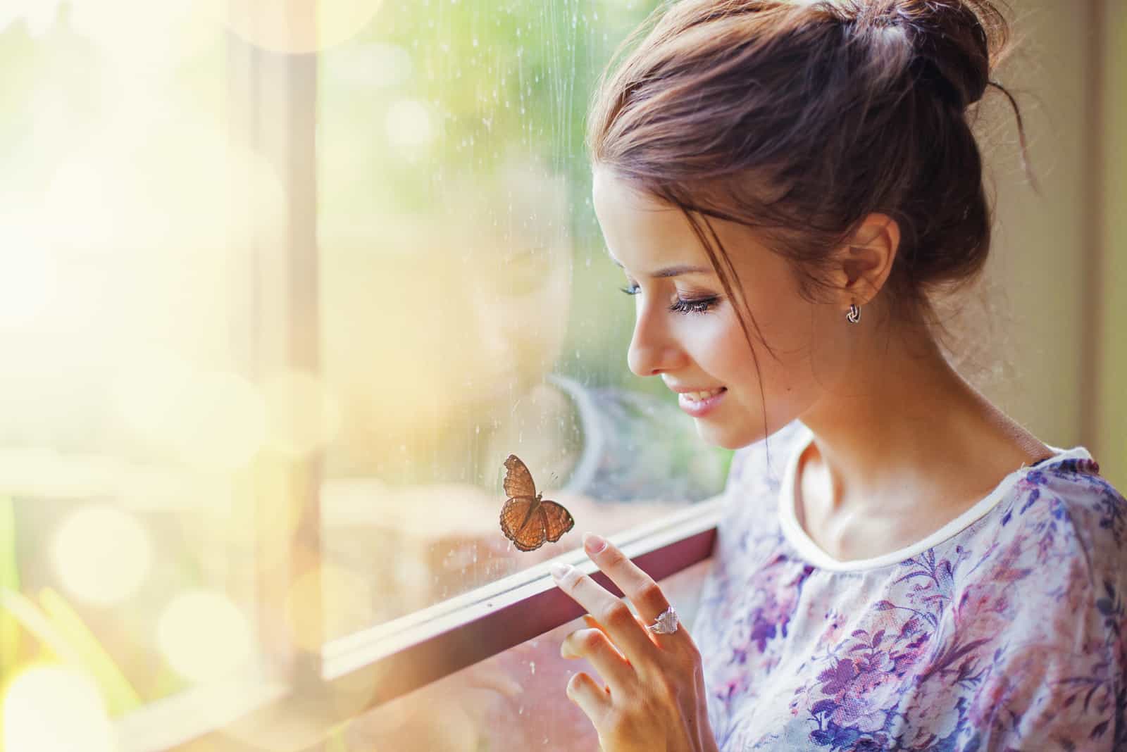 a beautiful woman sitting by the window touching a butterfly