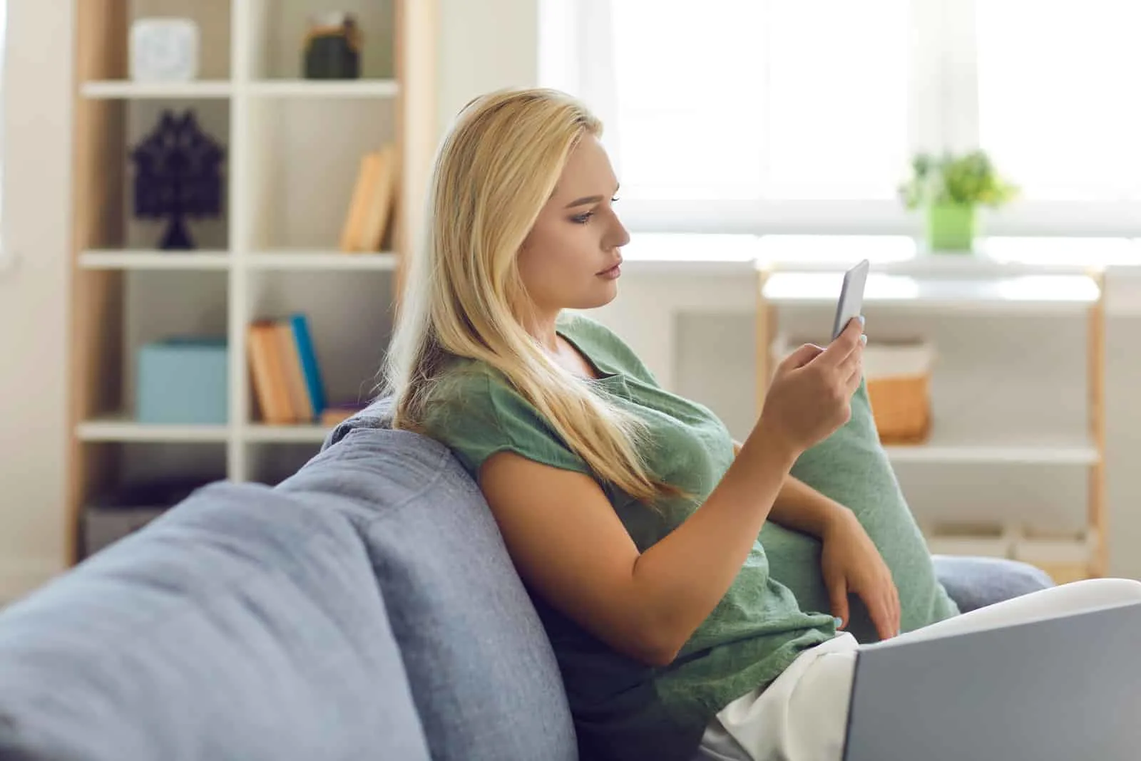 a beautiful woman with long blonde hair is sitting on the couch holding a phone in her hand