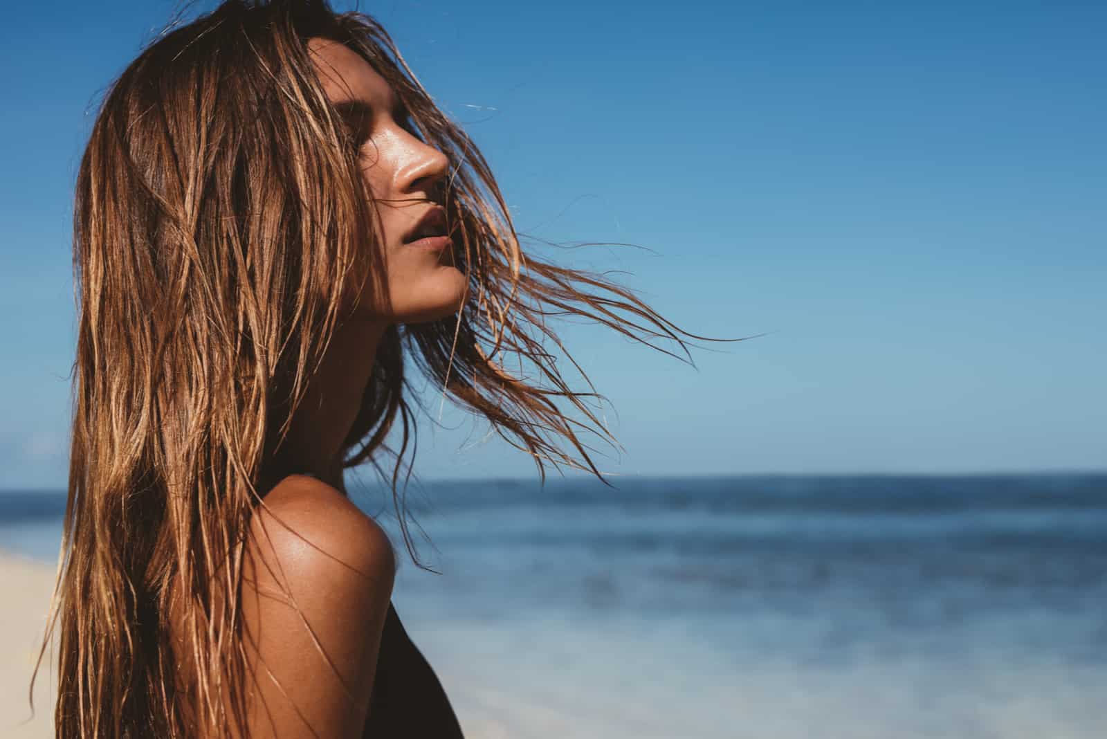 a beautiful woman with long brown hair stands on the beach