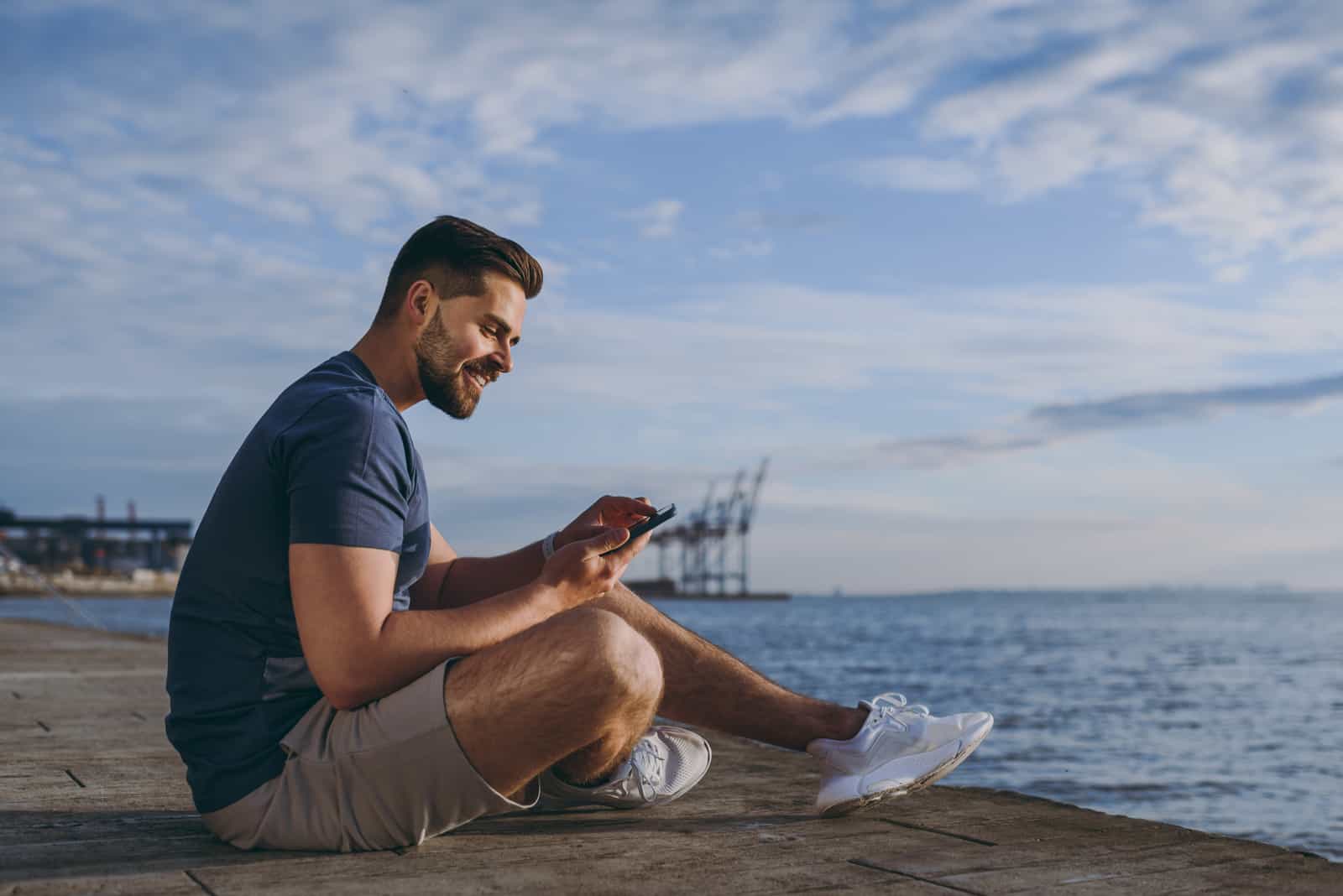 un hombre se sienta en la playa y llama por teléfono