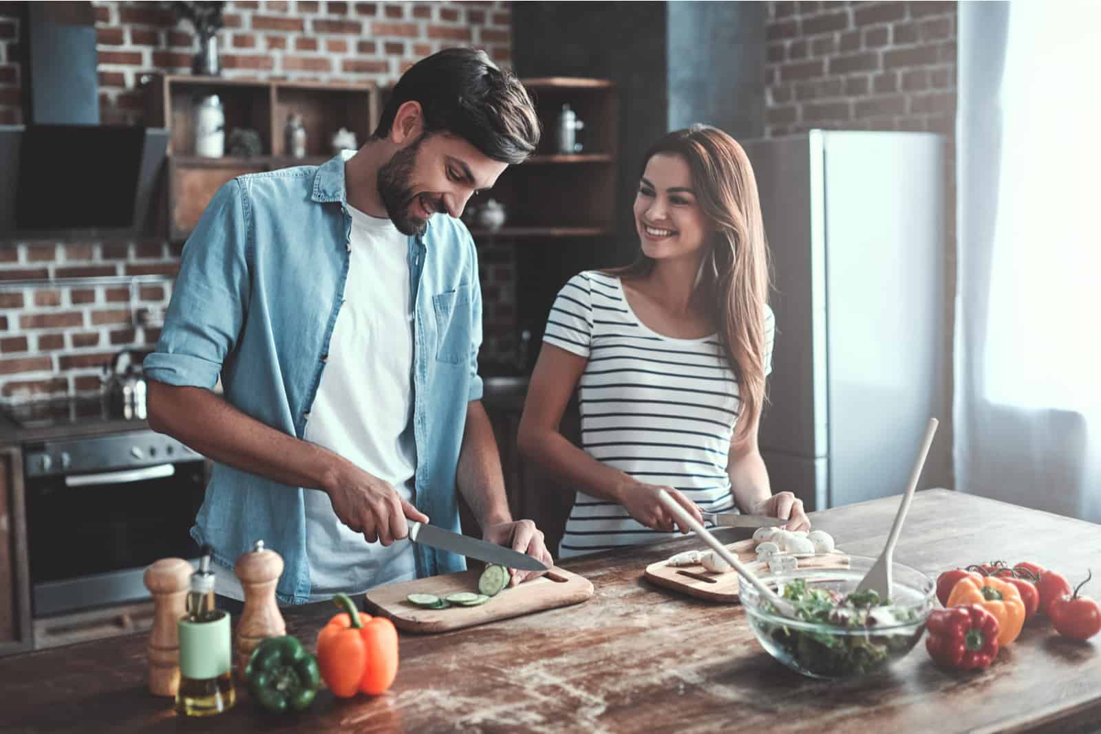 a smiling man and woman cooking together in the kitchen