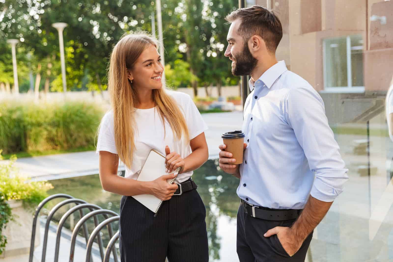 a smiling man and woman stand outdoors and talk