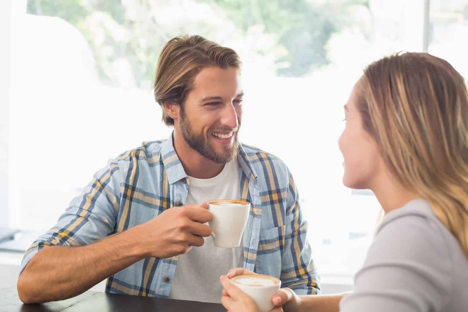 a smiling man holds a cup in his hand and talks to a woman
