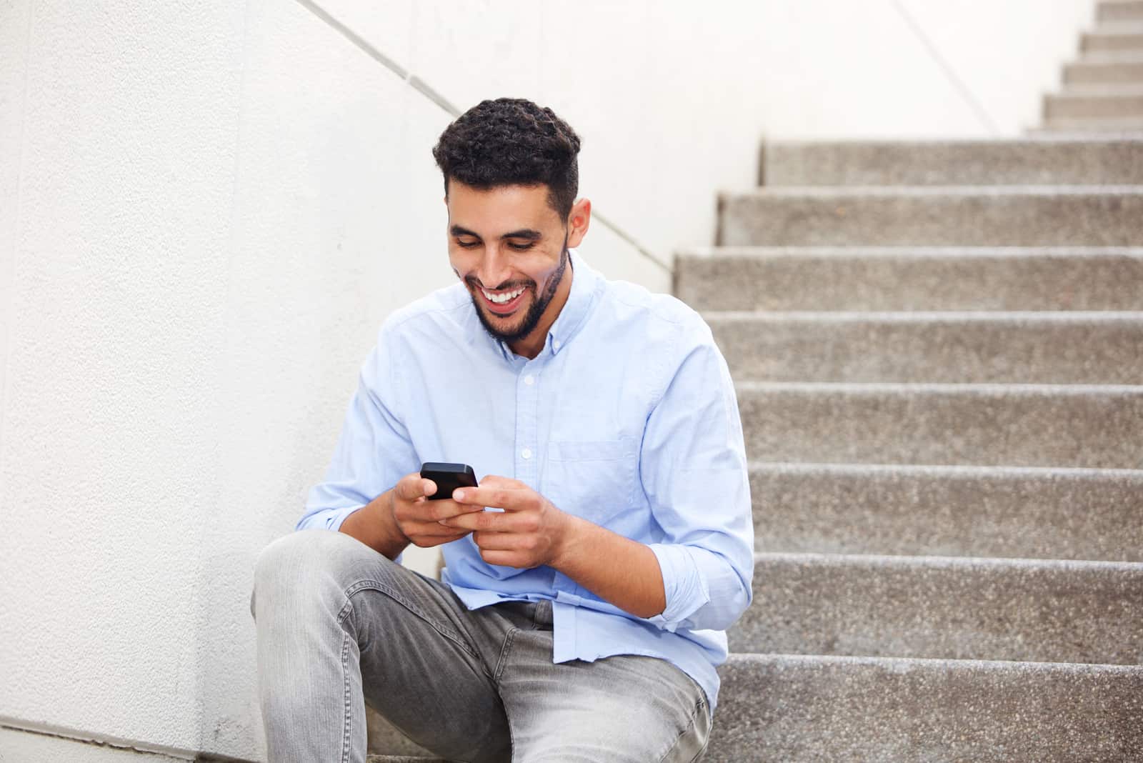 un uomo sorridente si siede sulle scale e abbassa i tasti del telefono