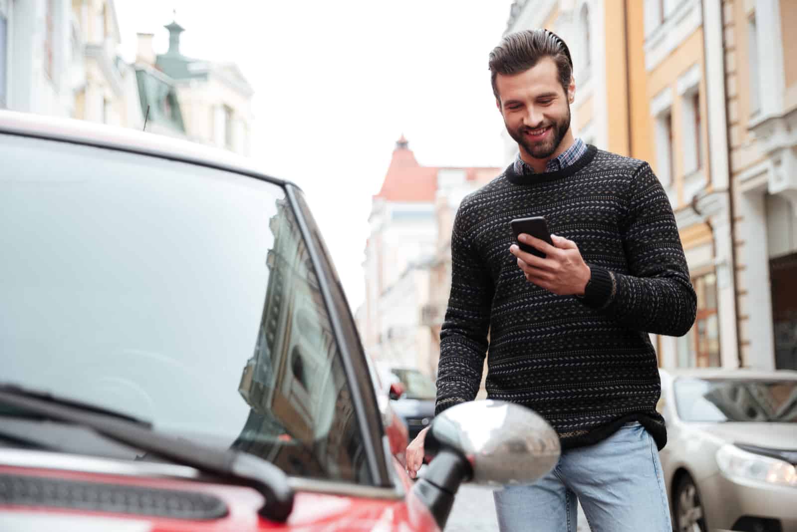a smiling man stands next to a car and buttons on the phone