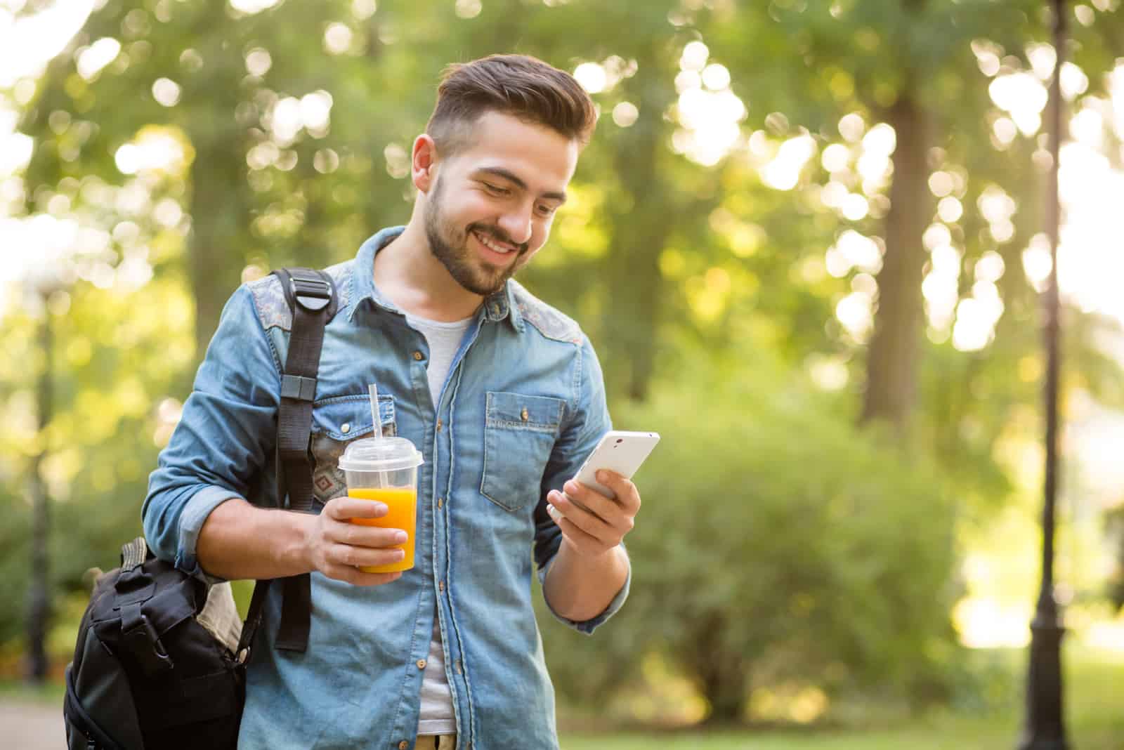 um homem sorridente caminha pelo parque e abotoa o telefone