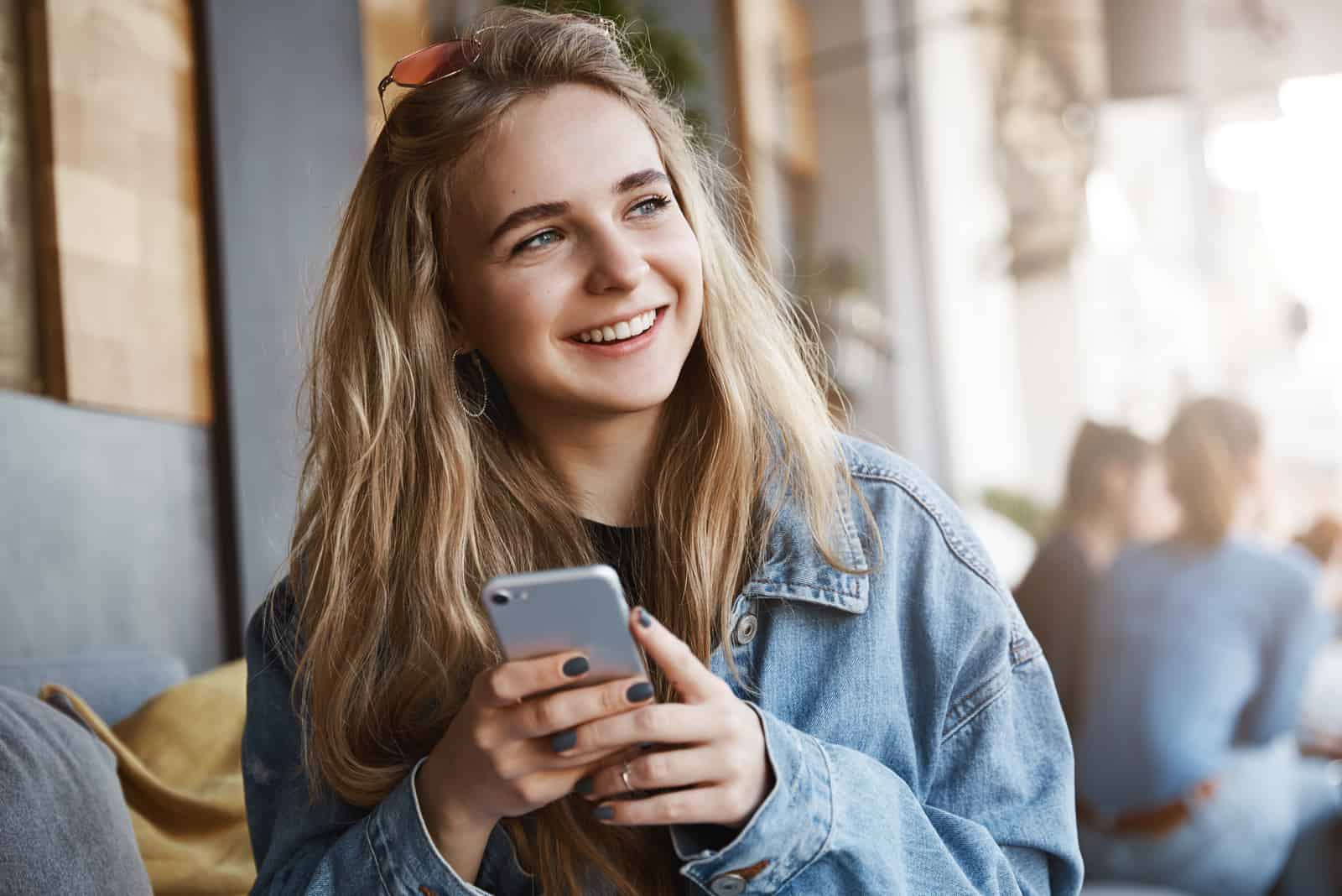 a smiling woman looks away and holds the phone in her hand