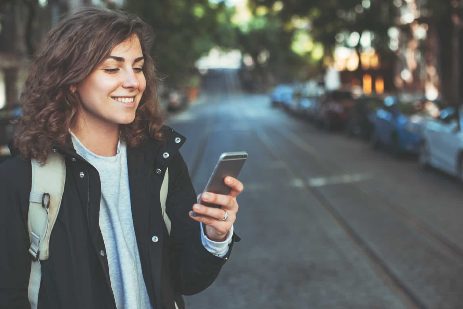 a smiling woman standing in the street and buttoning the phone