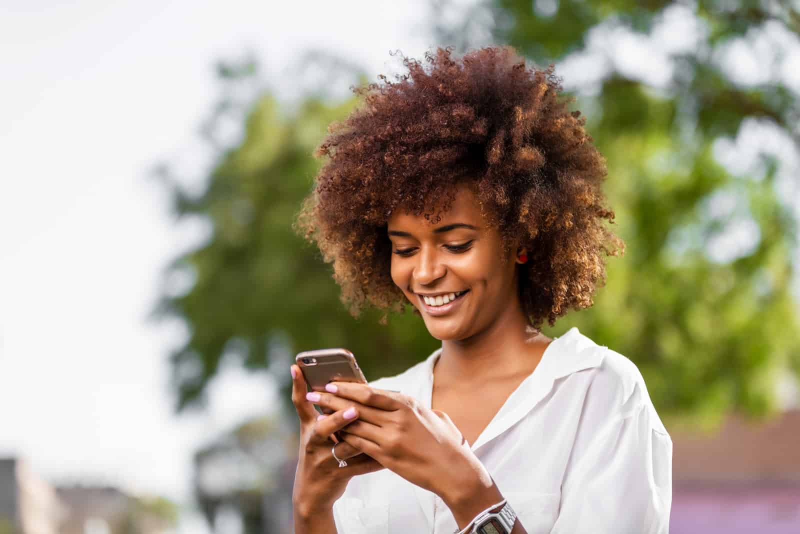 a smiling woman with frizzy hair holds a phone in her hand